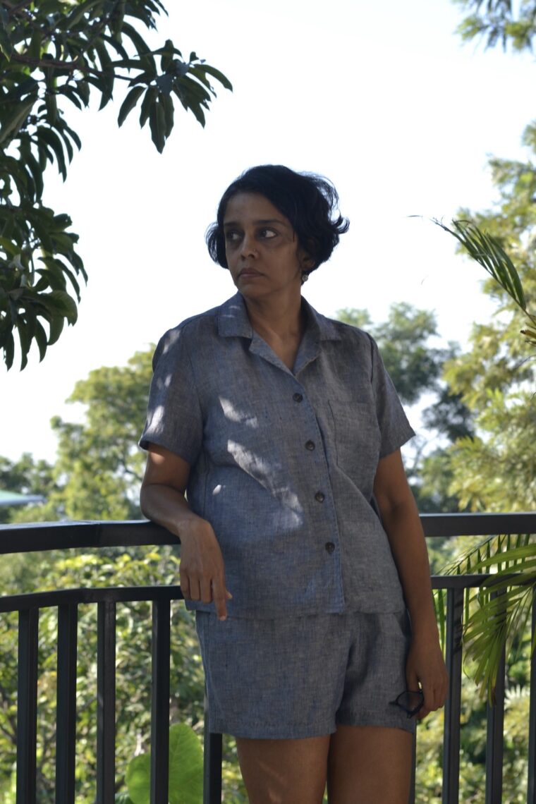 Woman leaning against a railing wearing a button up pajama shirt and pajama shorts