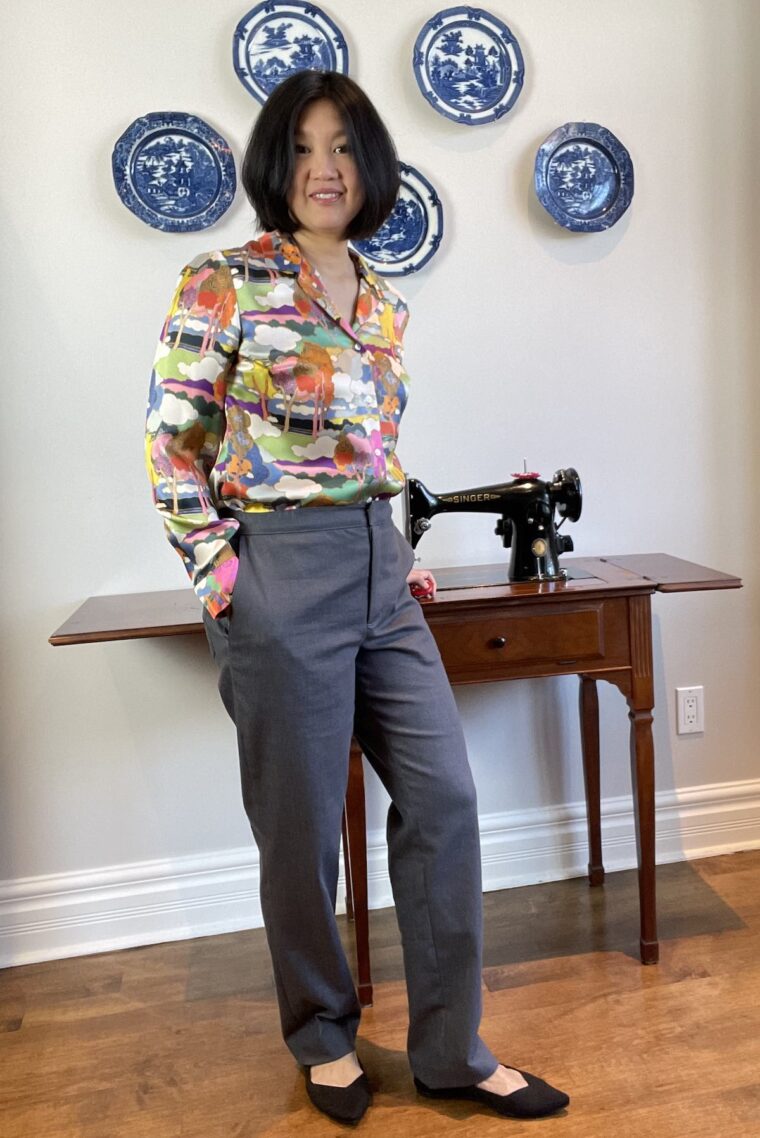 Woman wearing grey trousers standing in front of an antique sewing machine