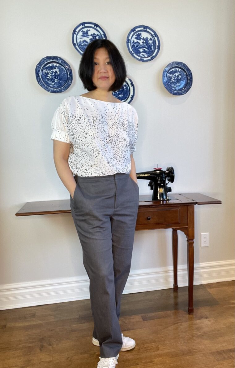 Woman wearing grey trousers standing in front of an antique sewing machine