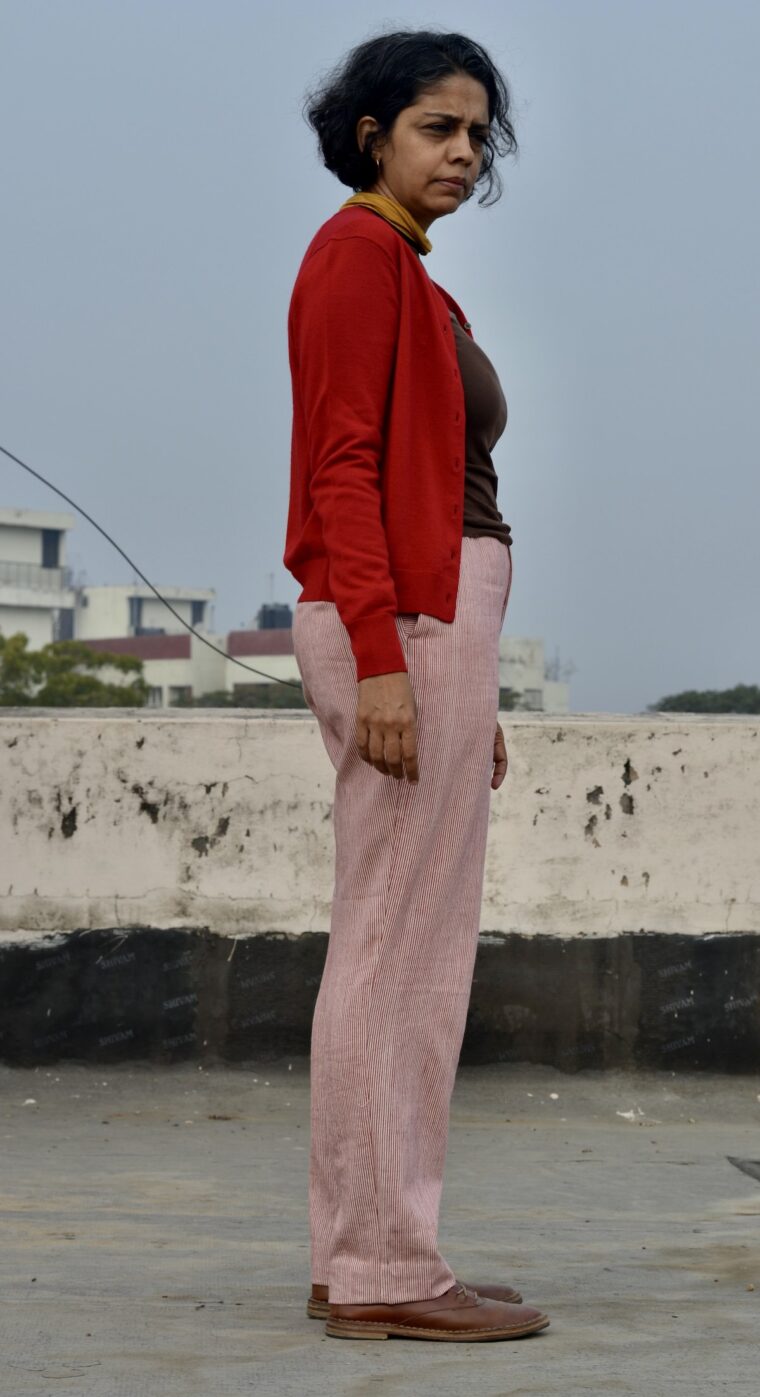 Side view of woman standing in red and white trousers, wearing a brown sweater and a red cardigan.