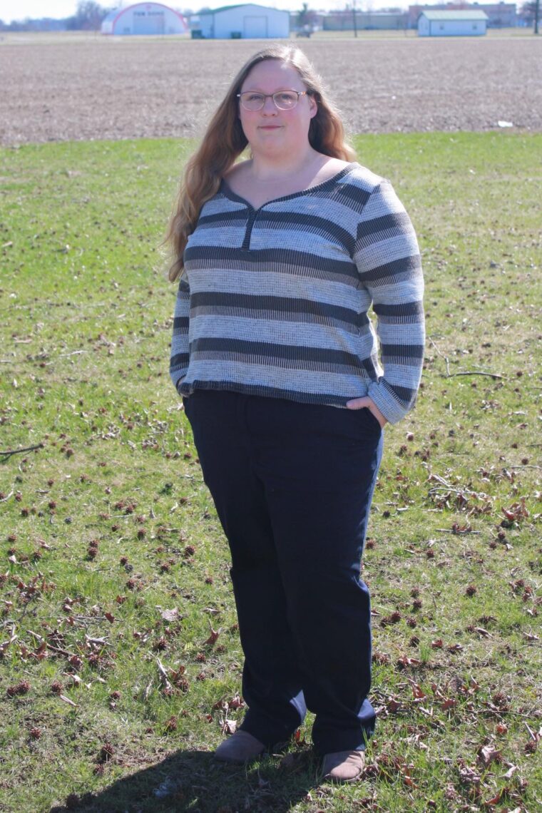 Woman standing outside in a striped knit henley shirt with long sleeves and navy pants