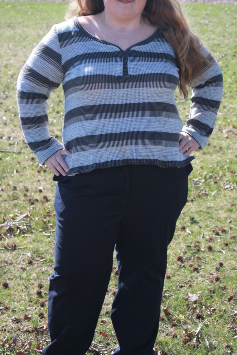 Close up of a woman standing outside in a striped knit henley shirt with long sleeves and navy pants
