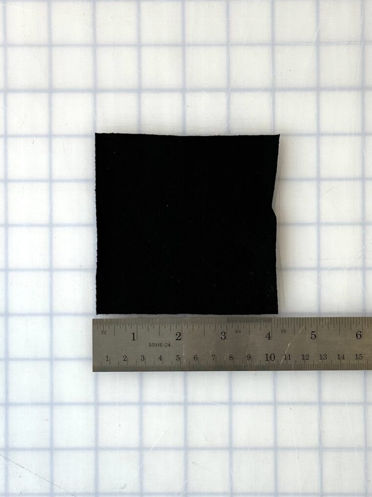 A square of black knit fabric cut to 4 inches by 4 inches. A silver ruler is under the fabric showing the measurement.