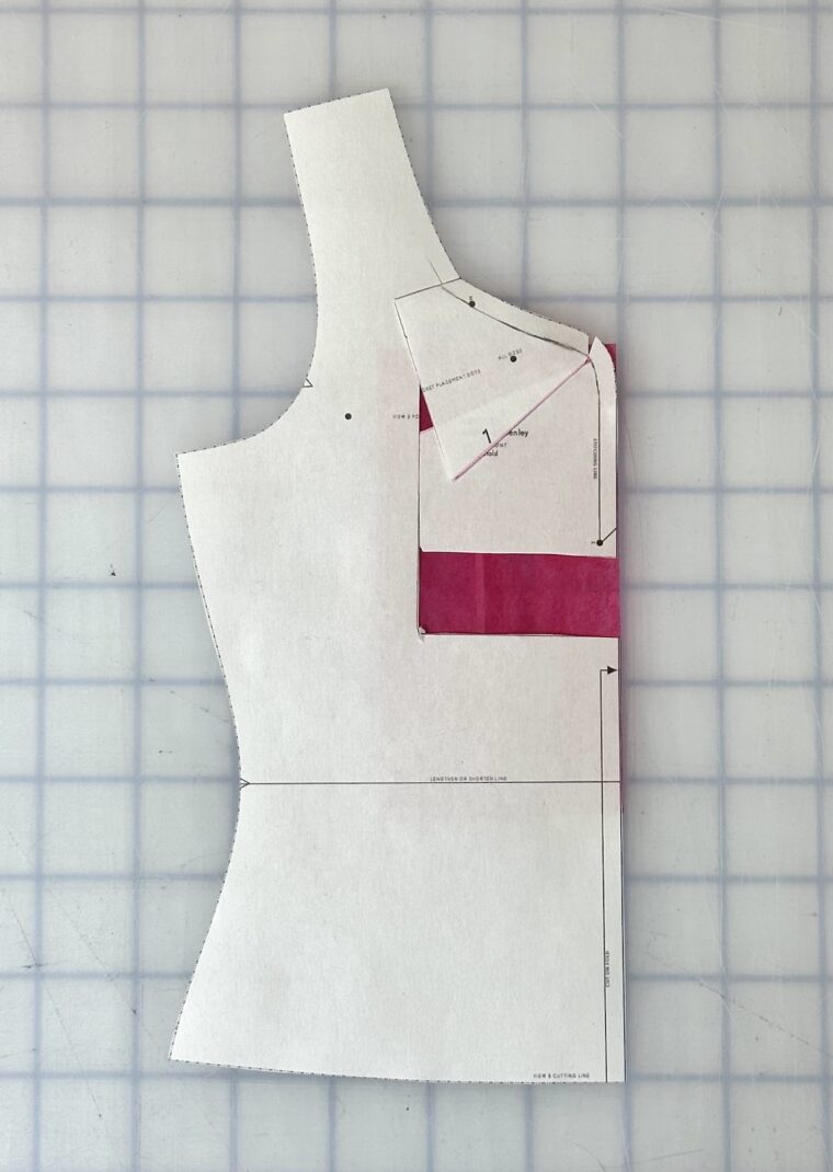 A front bodice pattern piece. I rectangle as been drawn around the center front neckline. The rectangle has been shifted up. The top of the rectangle has been angled to blend with the original neckline. Pink paper has been placed under the open areas caused by shifting the rectangle.