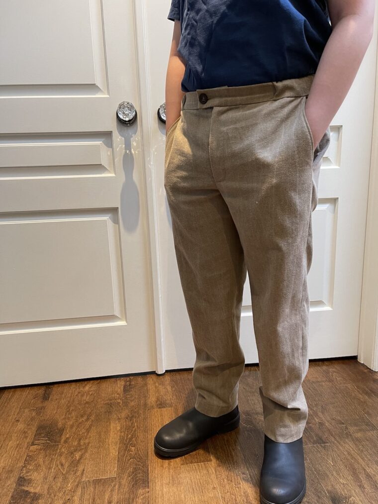 Side view of a young man wearing tan trousers and navy blue top. Picture is from the shoulders down.His hands are in his pocket.