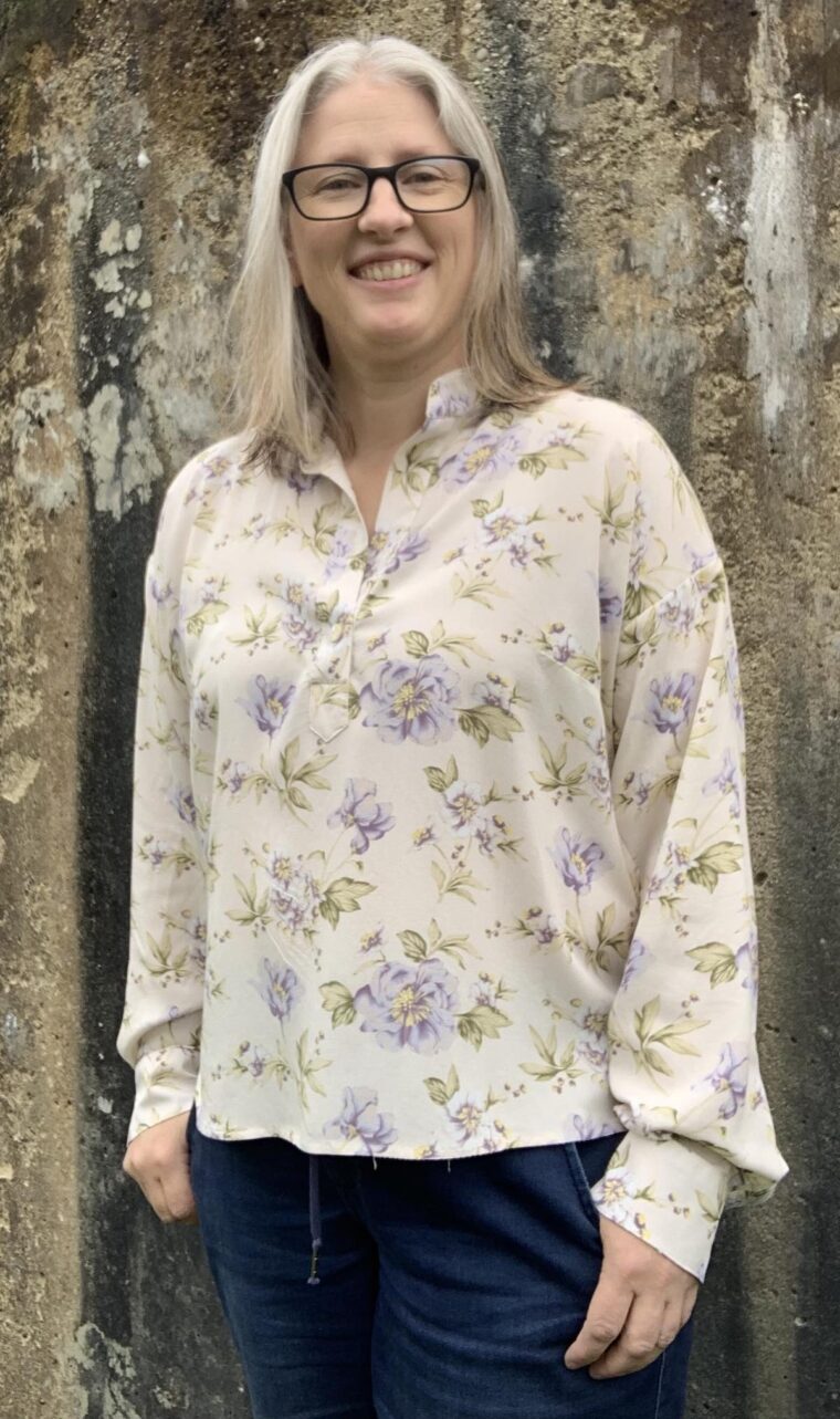 Smiling woman wearing a pullover long-sleeve blouse made in a drapey floral fabric.