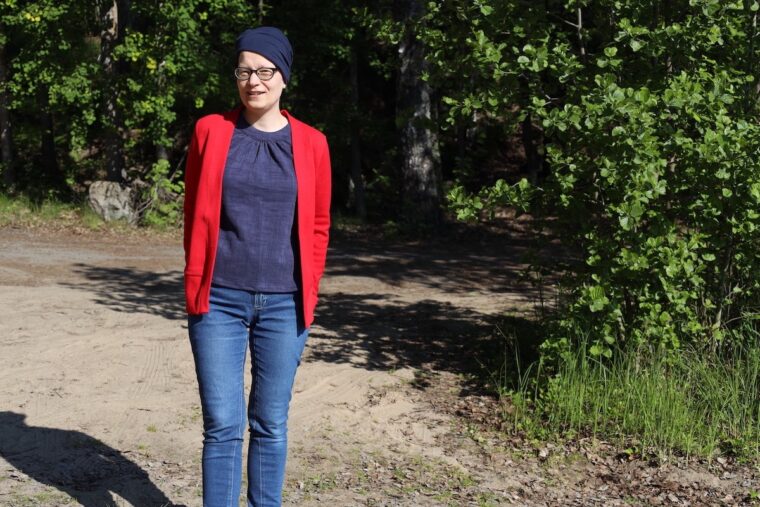 Woman is standing outside and smiling. She is wearing a navy halter top layered under a red cardigan and jeans.