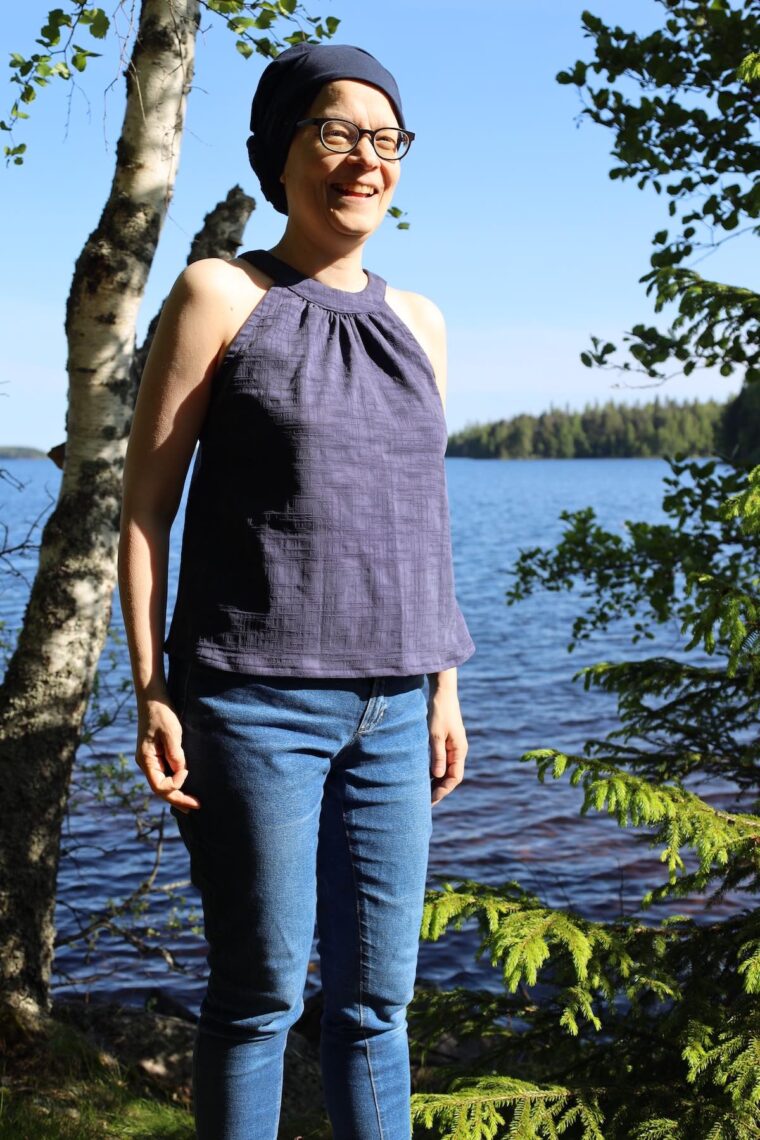 Woman is standing outside and smiling. She is wearing a navy halter top and jeans.