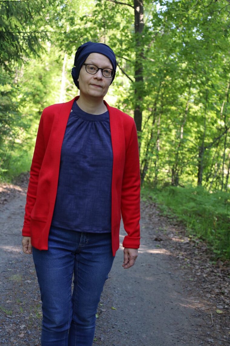 Woman is walking in the woods. She is wearing a navy halter top layered under a red cardigan and jeans.