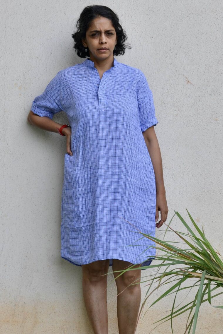 Woman wearing blue linen Santa Rosa Dress. She is standing outside in front of a white wall.