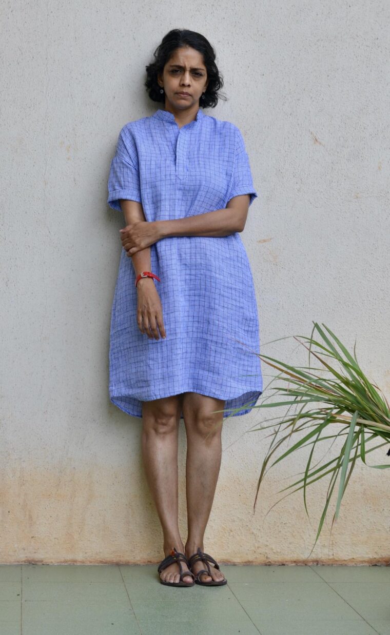 Woman wearing blue linen Santa Rosa Dress. She is standing outside in front of a white wall.