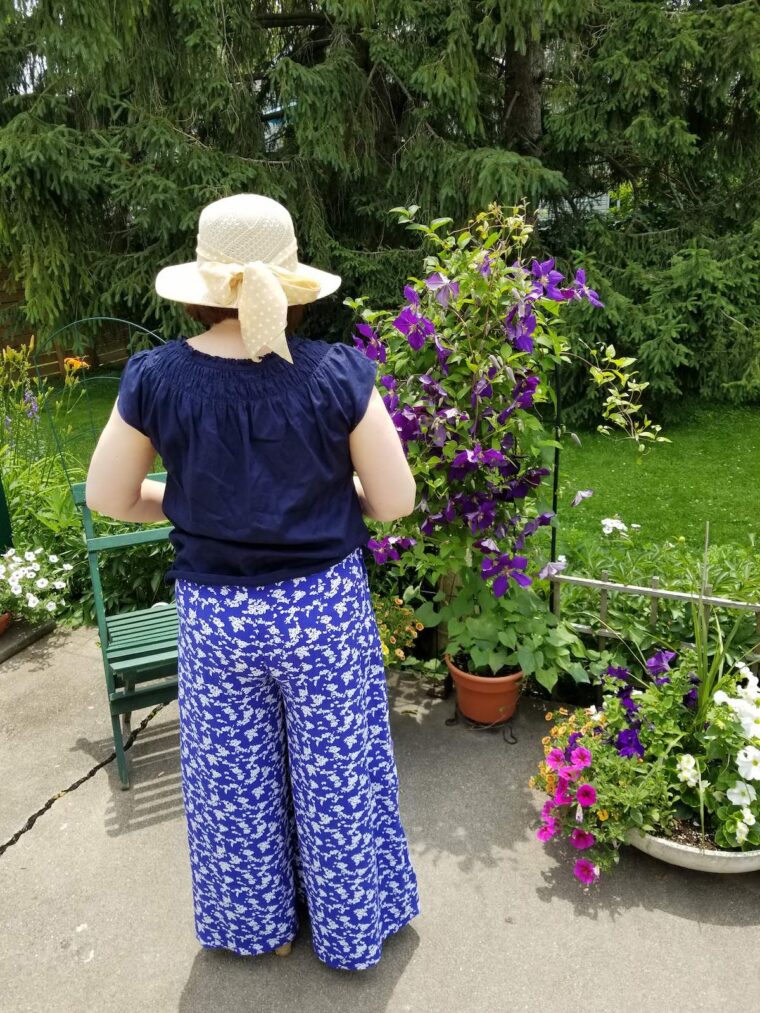 Back view of woman wearing wide-legged trousers with a navy shirt and straw sunhat.