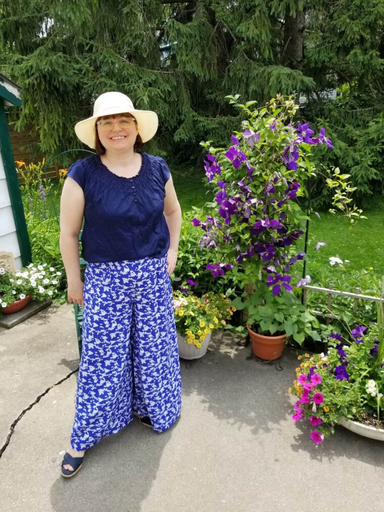 Woman wearing wide-legged trousers with a navy shirt and straw sunhat.