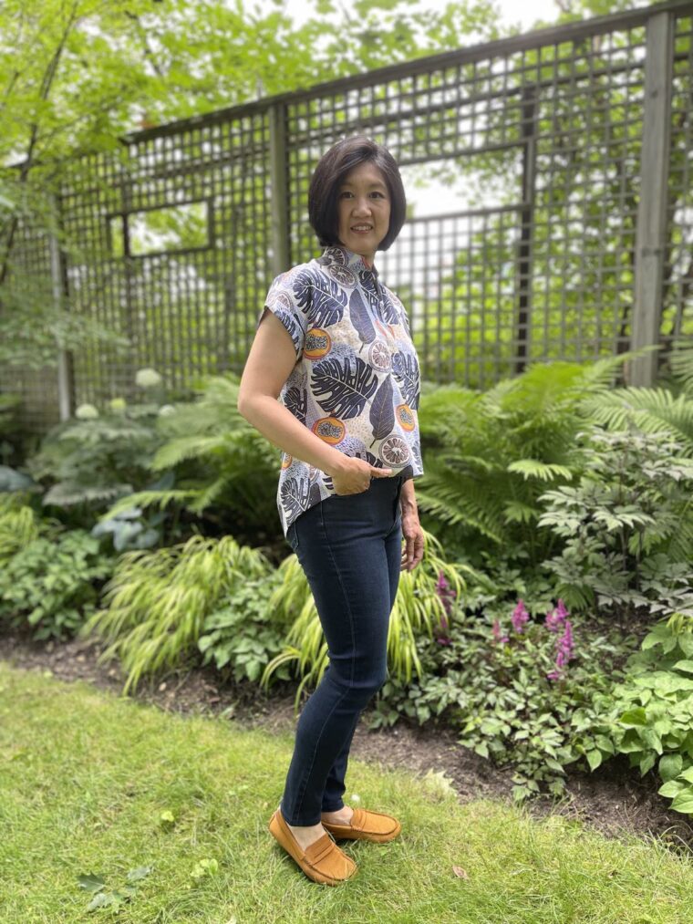 Side view of a woman standing in a backyard wearing a Santa Rosa top and jeans
