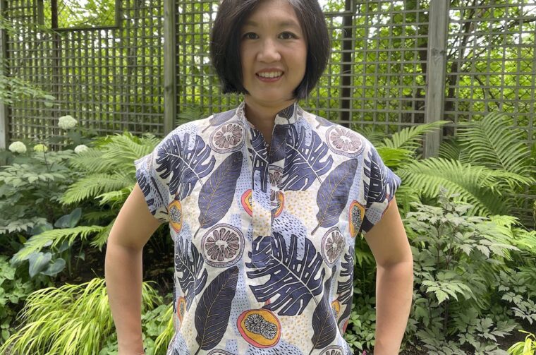 Close up of a woman standing in a backyard wearing a Santa Rosa top and jeans