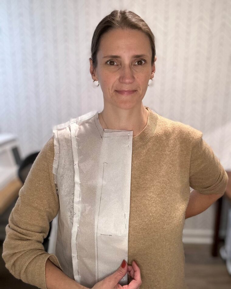 Close-up of woman wearing a tan sweater. On top of her sweater she is wearing a tissue sewing pattern that has been pinned together.